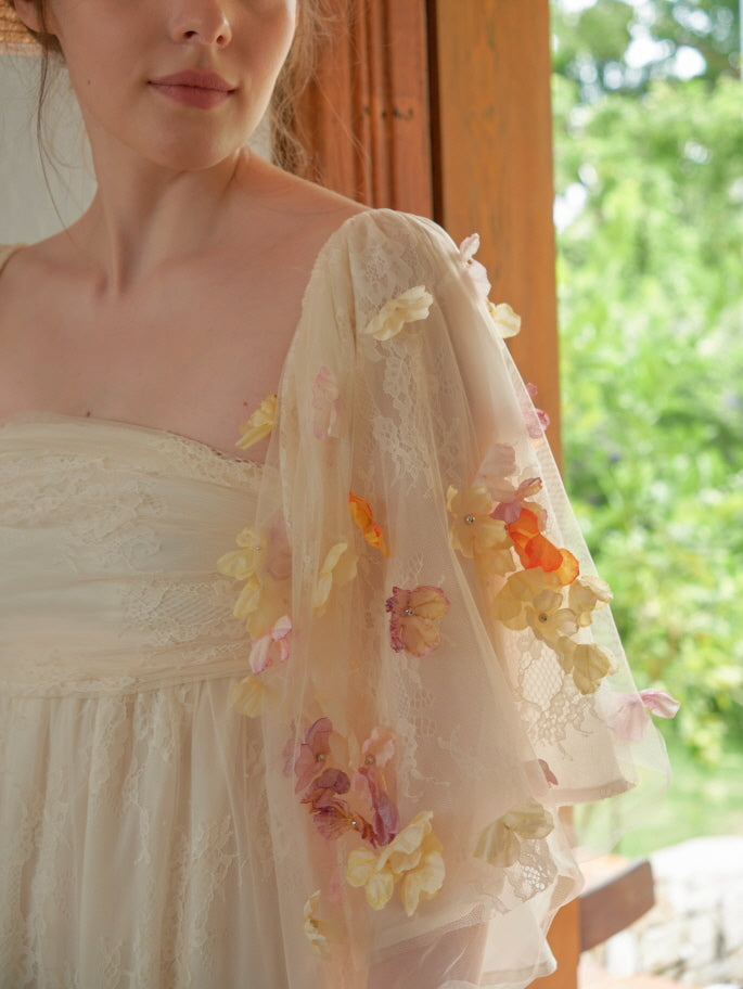 A close-up of a woman wearing a fairycore-style ivory lace dress with sheer floral-embroidered sleeves, exuding a soft vintage elegance.