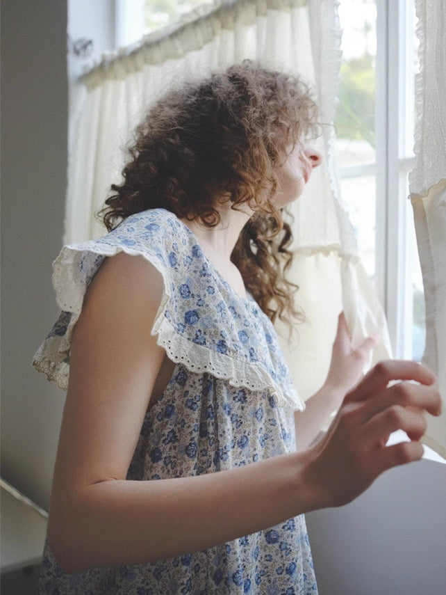 Wearing a vintage-style floral loungewear dress, the model gazes out the window with a dreamy expression, evoking a quiet cottagecore day.