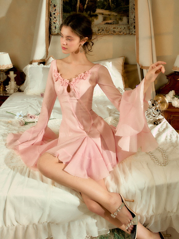 A model in a romantic pink mini dress with floral trim and bell sleeves poses elegantly, evoking fairytale charm and coquette princess beauty.