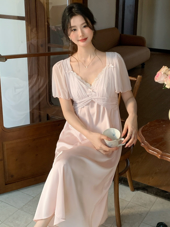 Sitting in a vintage-style chair, the model wears a pink fairycore loungewear dress with flutter sleeves, holding a teacup in a cozy, romantic setting.