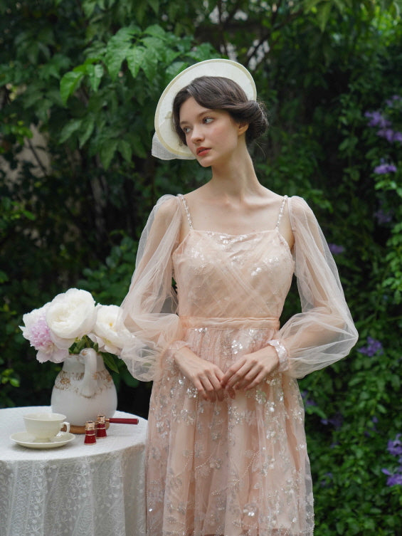 Model stands beside a tea table in a blush sequin dress with sheer puff sleeves, embodying romantic vintage elegance and soft fairycore charm.