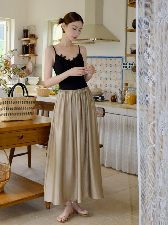 A woman stands in a vintage kitchen wearing a romantic outfit with a black floral-trim camisole and a flowing beige skirt in soft cottagecore style.
