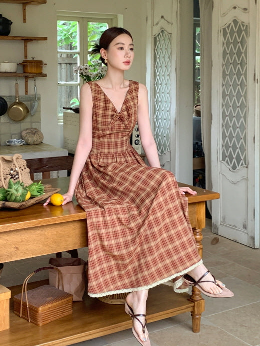 A woman sits on a wooden table in a red check vintage dress with lace trim, evoking a cozy cottagecore kitchen mood with a romantic vibe.