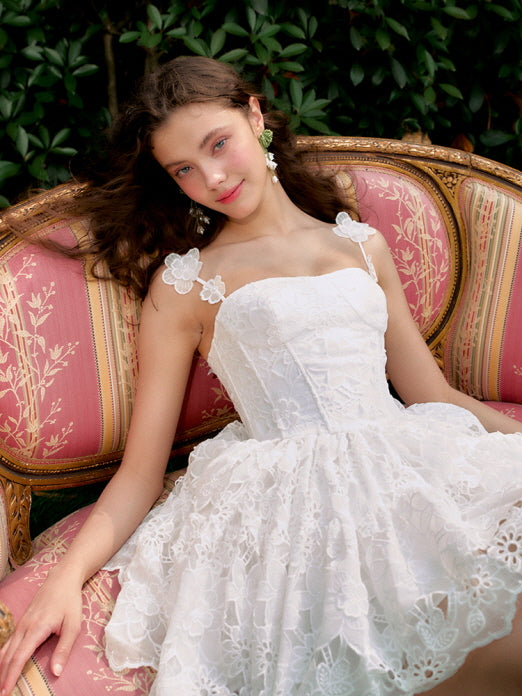 A close-up of a young woman reclining on a vintage pink sofa, her floral lace dress and soft smile capturing a dreamy princesscore mood.