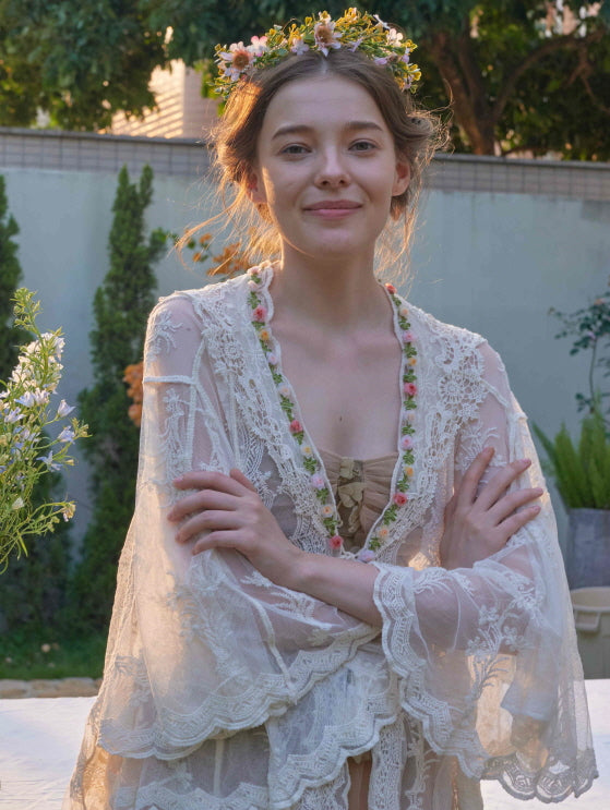 Close-up of a smiling woman in a sheer floral lace robe with embroidery trim, styled with a flower crown for a soft fairycore mood.