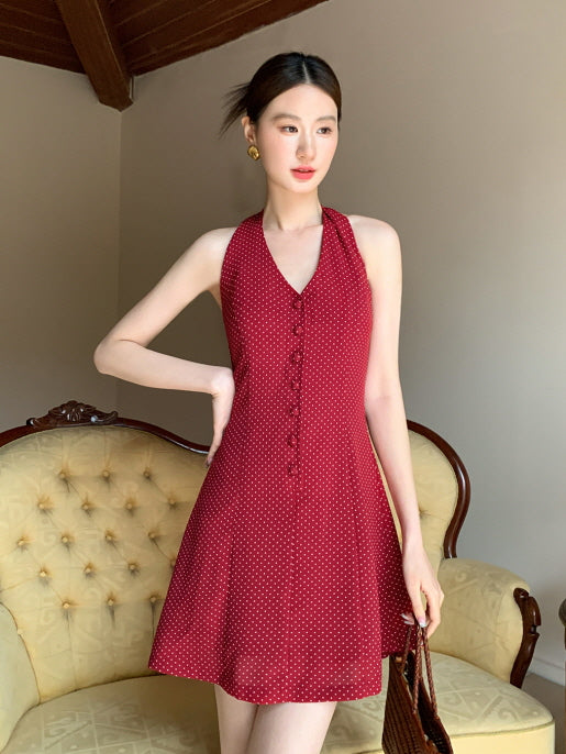 A young woman poses in a vintage-inspired red halter dress with tiny white polka dots, exuding a charming princesscore summer look.