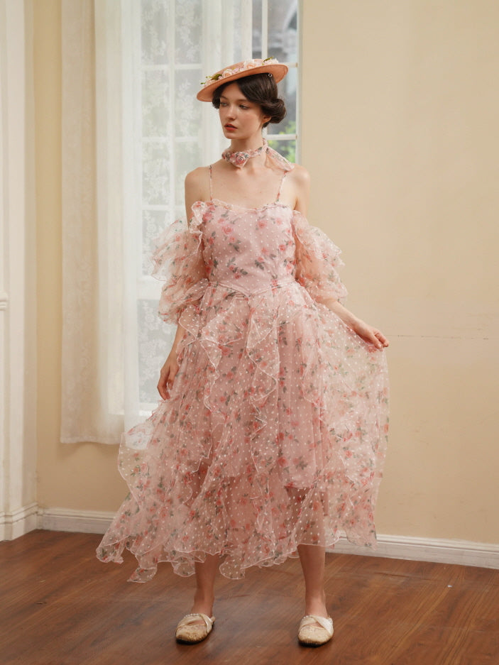 A woman in a romantic pink floral ruffle dress poses gracefully by a sunlit window, exuding soft elegance and fairycore charm.