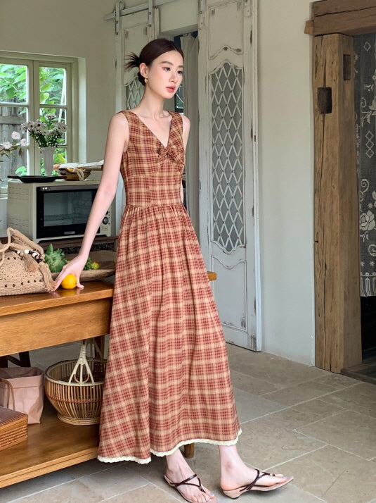 Standing by a rustic table with lemons and a woven bag, a woman wears a sleeveless plaid dress perfect for vintage cottagecore styling.