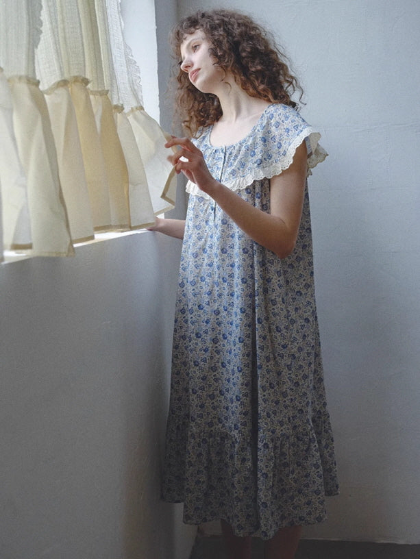 A woman in a blue floral cotton nightgown gazes out the softly lit window, embodying a peaceful morning in a romantic cottagecore setting.