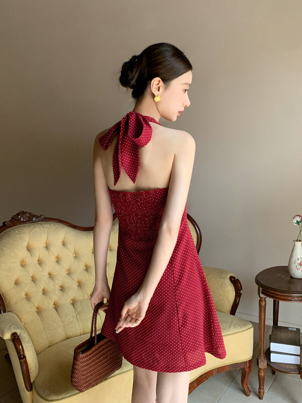 Back view of a woman in a red halter polka dot mini dress tied with a large bow, styled in a romantic fairycore outfit with a woven bag.