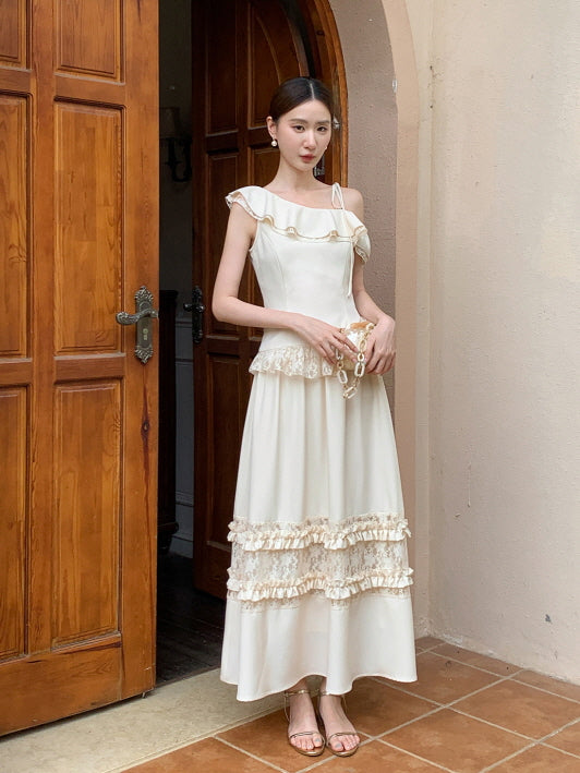 The model poses in a vintage cream outfit featuring a ruffle one-shoulder top and layered skirt, styled with a pearl bag in a romantic setting.