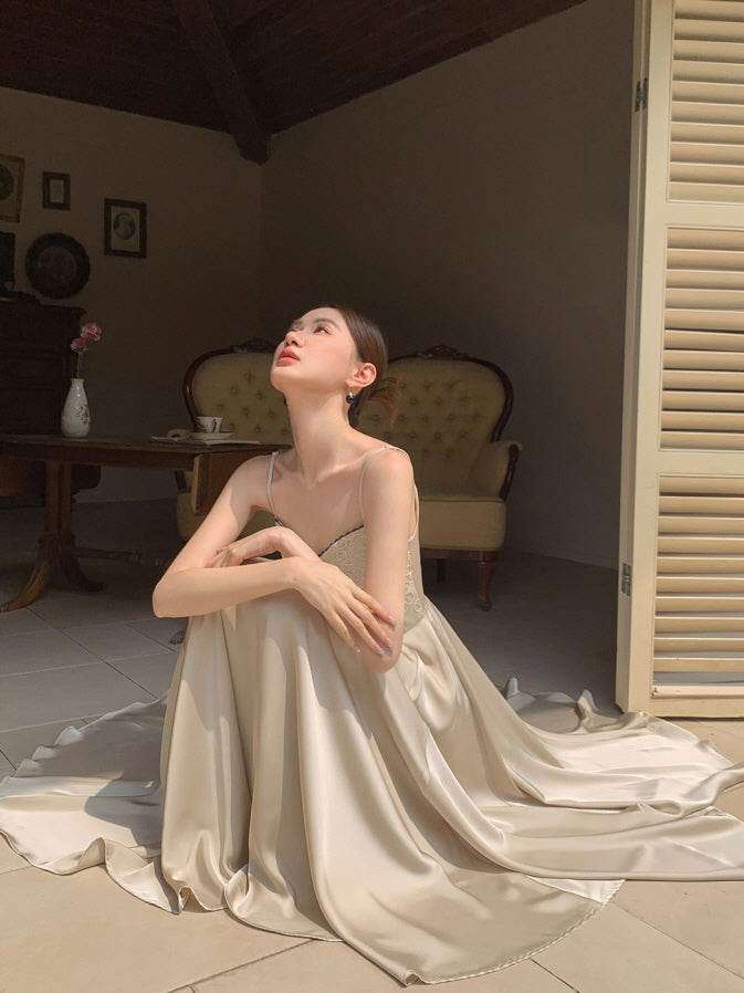 A woman in a vintage-inspired cream gown sits in soft sunlight, her flowy skirt spread around her, evoking a quiet fairytale moment.