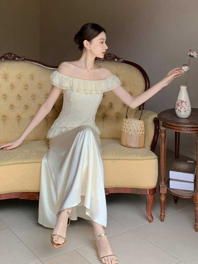 A woman sits gracefully on a vintage sofa wearing a cream off-shoulder ruffle top and satin skirt, styled in an elegant cottagecore interior.