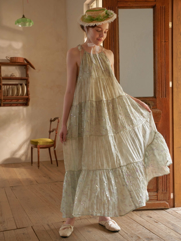 A woman gently holds the hem of her shimmering green tiered dress, styled with a lace bonnet in a softly lit fairytale-inspired room.