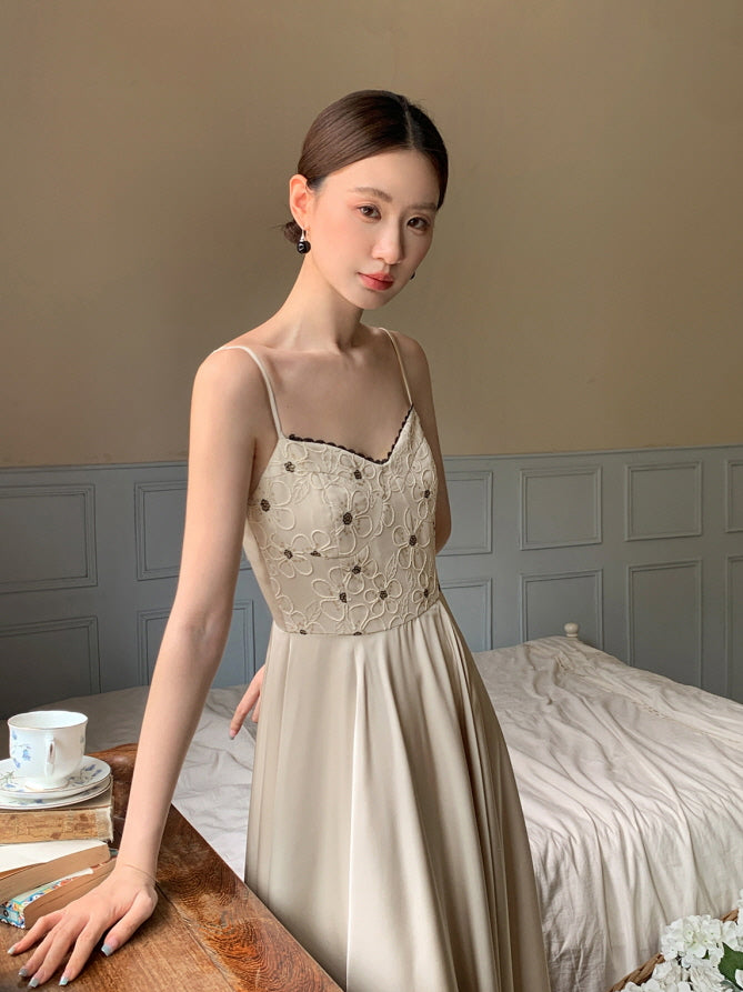Close-up of a romantic embroidered bodice with delicate straps, worn by a woman standing beside a wooden table in a dreamy cottagecore room.