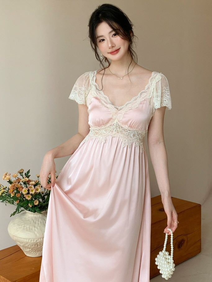 A model poses gracefully in a romantic pastel pink lace nightdress, holding a pearl mini bag with a cottagecore floral backdrop.