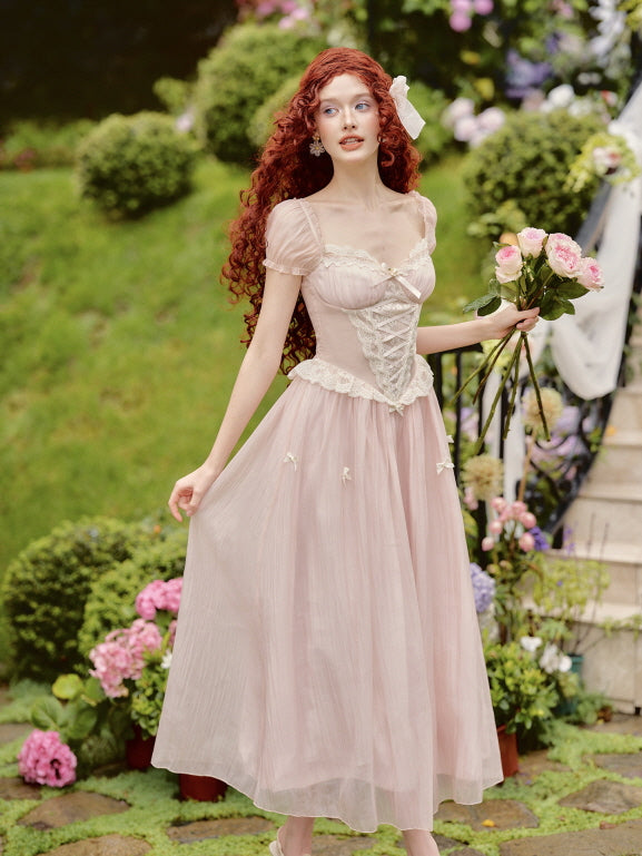 A young woman holds a bouquet of pink roses while wearing a fairycore-inspired light pink corset fairytale dress with lace-up detail, surrounded by floral garden scenery.