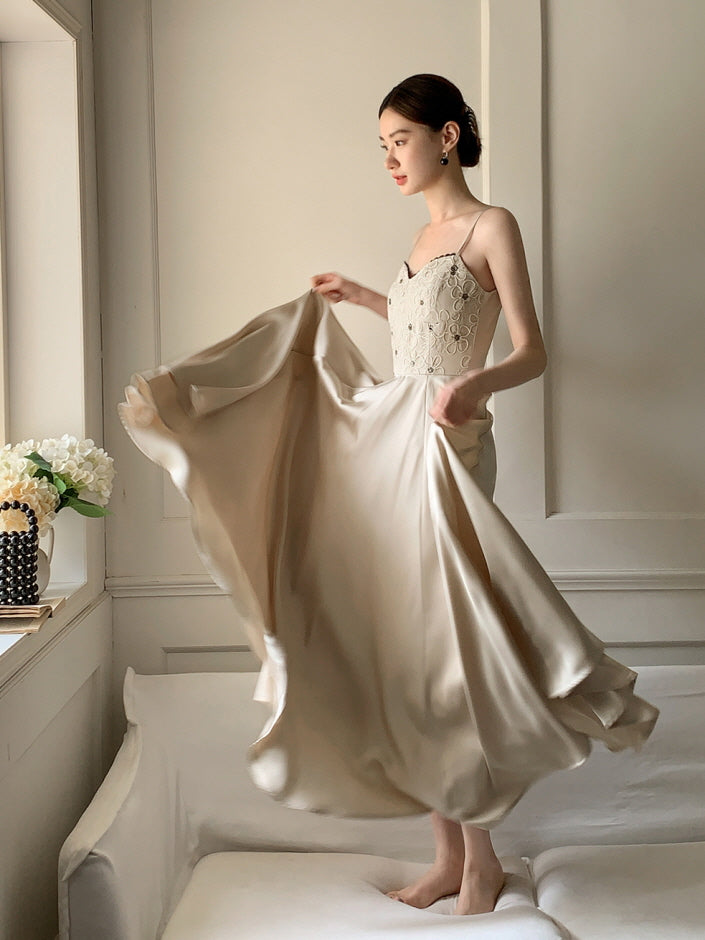 A woman twirls barefoot on a white sofa in a flowing beige dress, capturing a dreamy fairycore moment with soft movement and elegance.