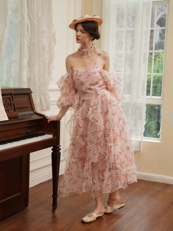A woman in a layered pink rose-print dress leans softly on a piano, capturing a serene and nostalgic fairycore moment by the window.
