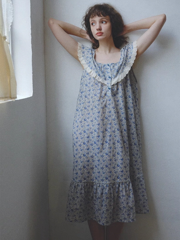 The model stretches softly in a blue floral nightgown with ruffled lace collar, embodying a calm, vintage-inspired morning in cottagecore style.