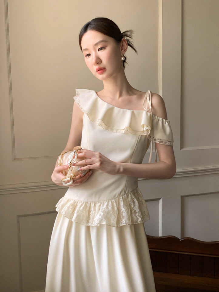 Wearing a cream off-shoulder top with lace frill and ribbon tie, the model holds a pearl-accented bag in a calm, vintage-inspired room.
