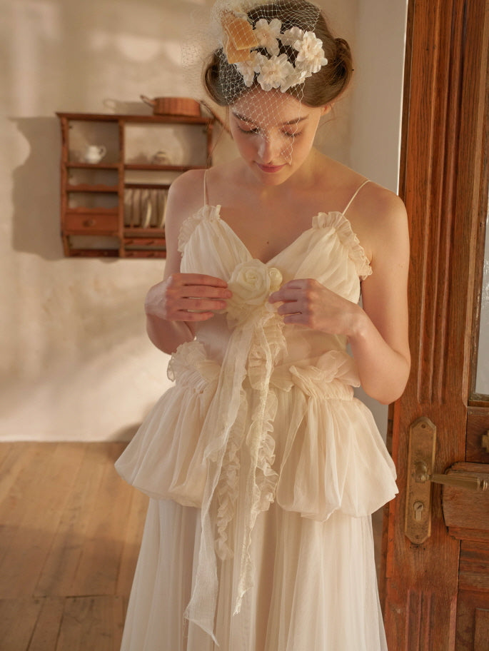 A woman stands indoors wearing a cream tulle two-piece dress with a ruffled peplum and rose detail, styled in romantic fairytale-inspired fashion.