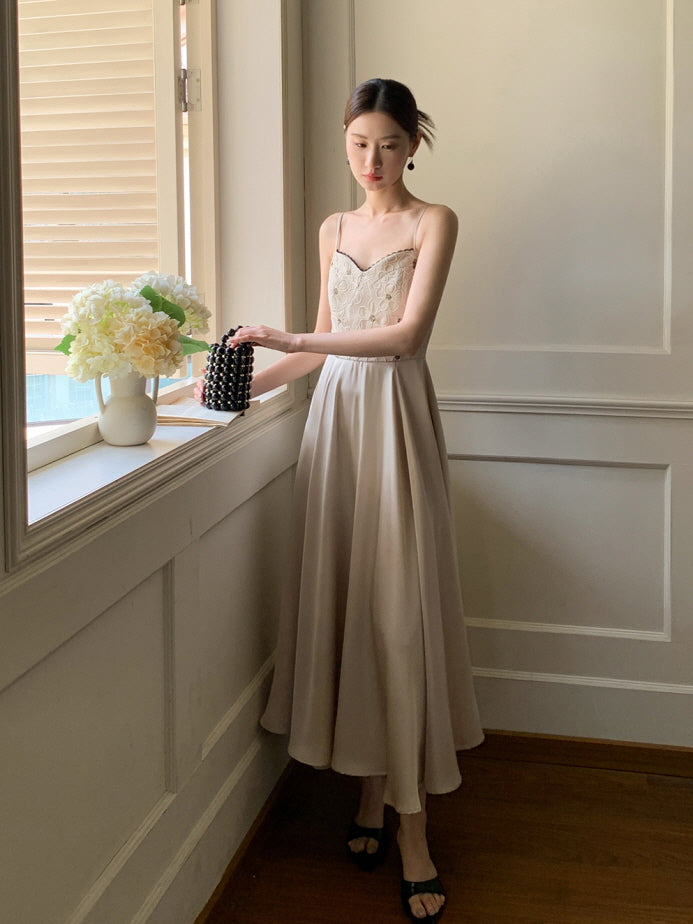 A woman in a soft beige summer dress stands by a window with hydrangeas, holding a beaded bag, radiating vintage elegance in a cottagecore interior.