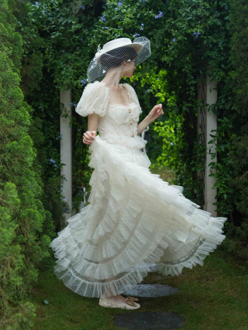 Model twirls mid-motion in a flowing ivory tiered gown with puff sleeves and a veiled hat, radiating whimsical fairytale grace in a garden arch.