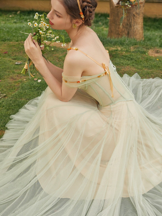 Model holding daisies while wearing a fairycore green corset dress with sheer off-shoulder straps and a dreamy vintage aesthetic look.