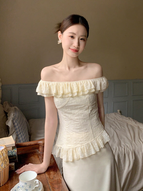 Smiling woman in an off-shoulder ivory blouse with ruffle details, styled in a romantic vintage bedroom with soft natural light.