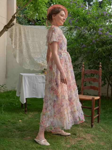 A side view of a woman in a flowing vintage-style princess dress with puff sleeves, walking through a dreamy garden in soft daylight.