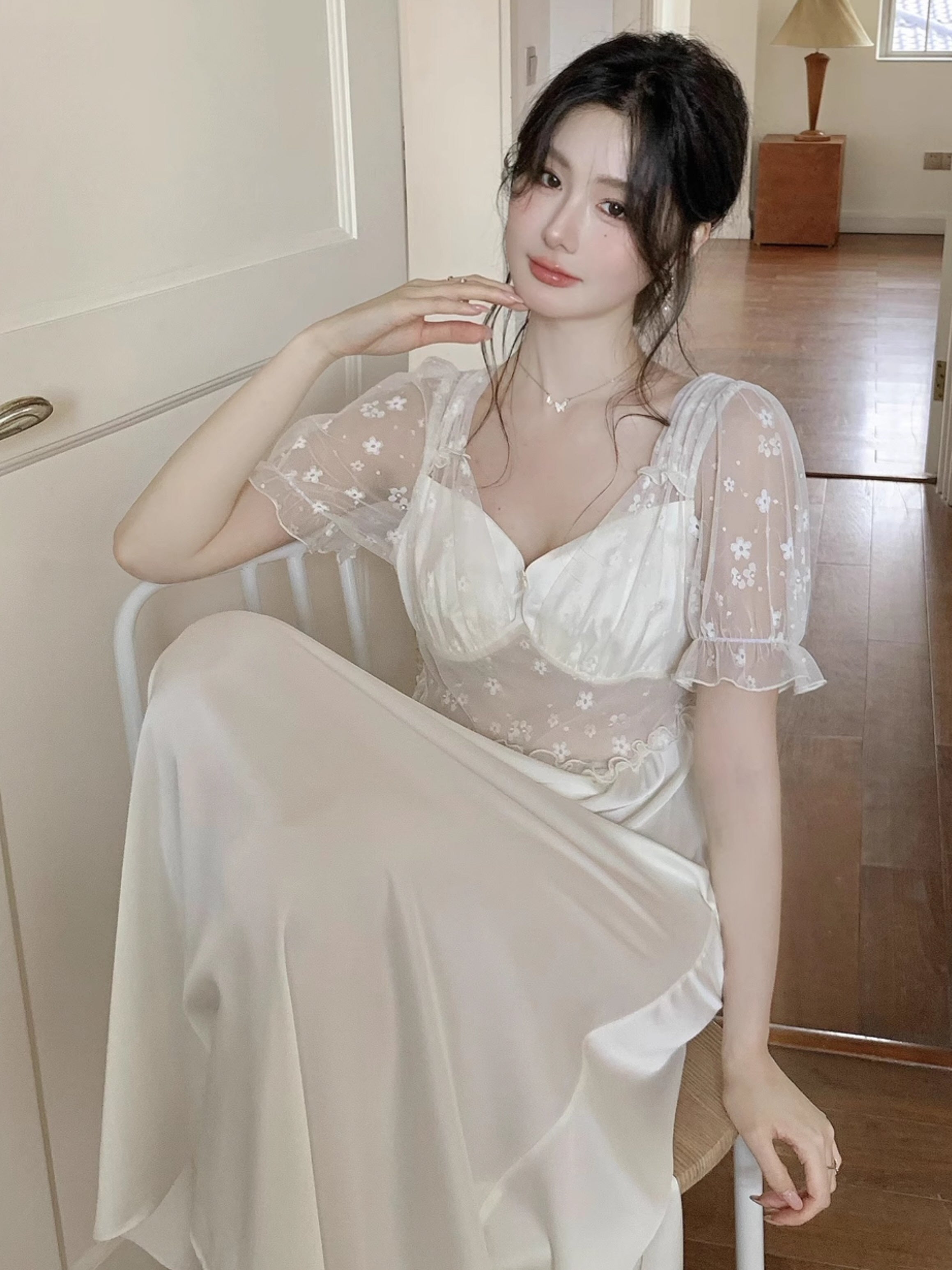 Woman sitting gracefully in a mesh romantic nightgown, featuring floral embroidery and princess-style details, styled in a quiet vintage interior.