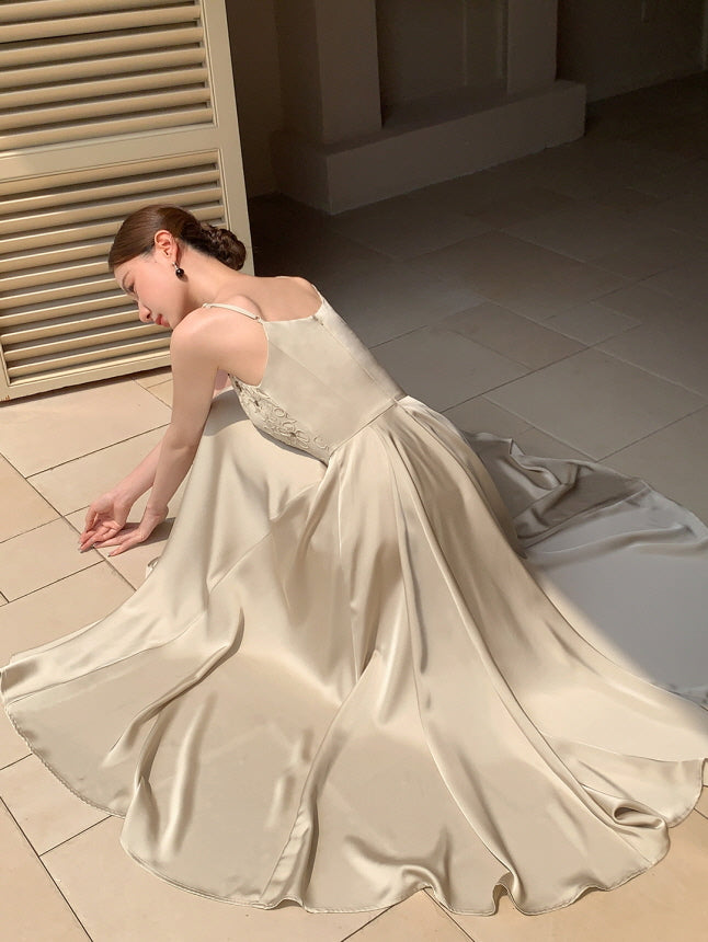 A woman sits gracefully on a tiled floor in a flowing satin dress, her back turned slightly, capturing a serene vintage fairytale aesthetic.