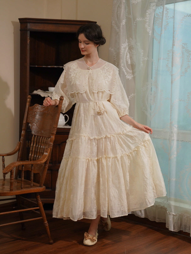 A woman in a tiered lace dress holds a wooden chair with one hand and lifts her skirt slightly, creating a graceful vintage cottagecore scene.