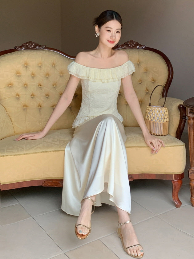 A woman poses elegantly on a vintage sofa wearing a flowing cream skirt and textured fairycore top, evoking a quiet, romantic charm.