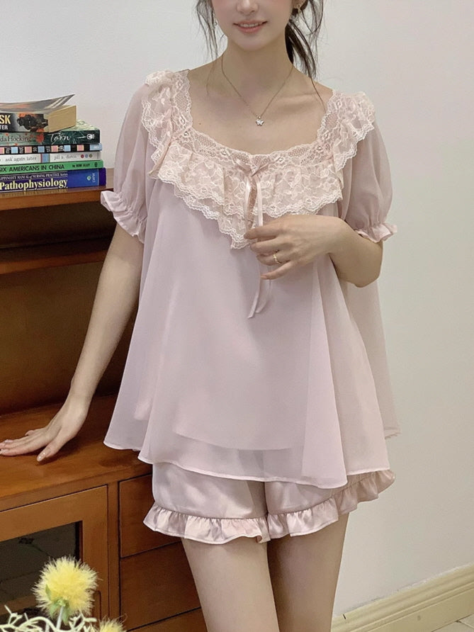 Model in a blush pink chiffon pajama set with ruffle shorts and lace neckline, standing beside a bookshelf in a cozy vintage room.