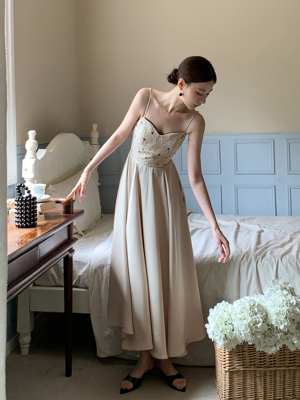 In a quiet cottagecore bedroom, a woman in a soft embroidered chic dress leans toward a rustic table, exuding timeless romantic elegance.