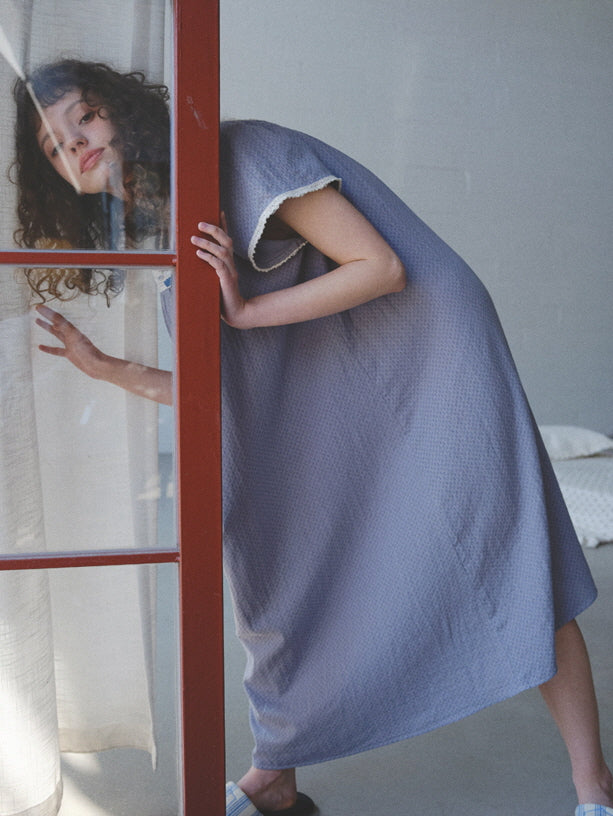 The model steps through a red-framed door in a lavender cotton nightgown with lace trim, creating a soft and nostalgic vintage mood.