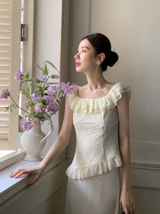 Side view of a woman in a textured ivory blouse with frill accents, gazing out the window beside a vase of pastel flowers in a cottagecore mood.