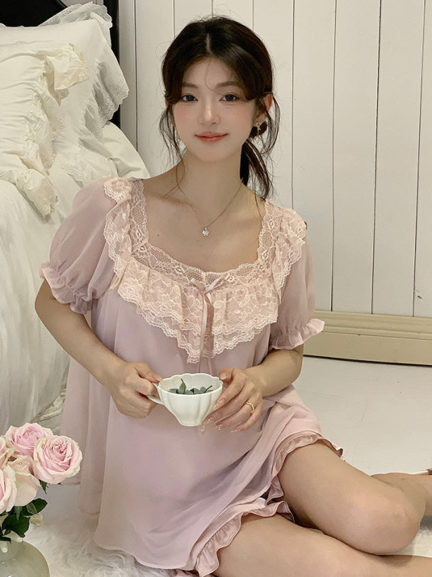 Model sitting on a white rug holding a teacup, dressed in a soft pink loungewear set with lace ruffle detail and fairycore elegance.
