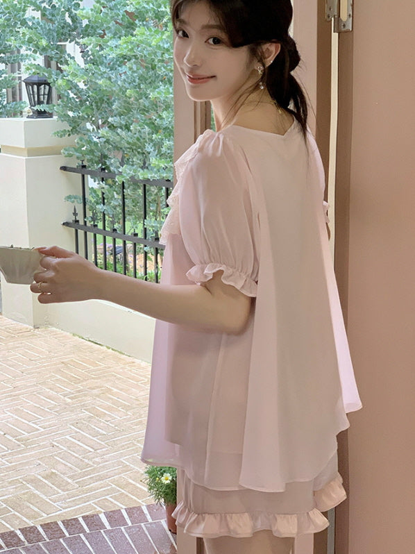 Woman smiling as she looks back by the doorway, wearing a pastel pink coquette cute pajama set with frilly hem and flowy chiffon top.