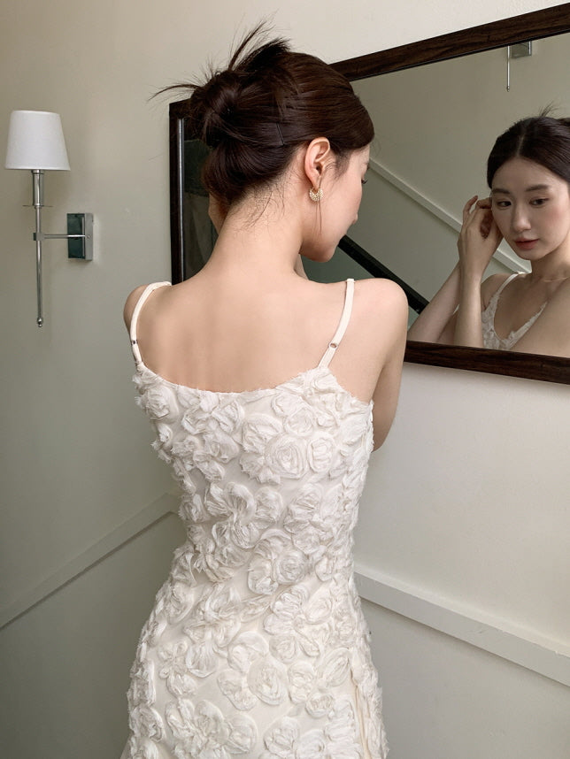 A close back view of a romantic ivory mini dress with 3D floral textures, as the model adjusts her earring in a softly lit vintage hallway.