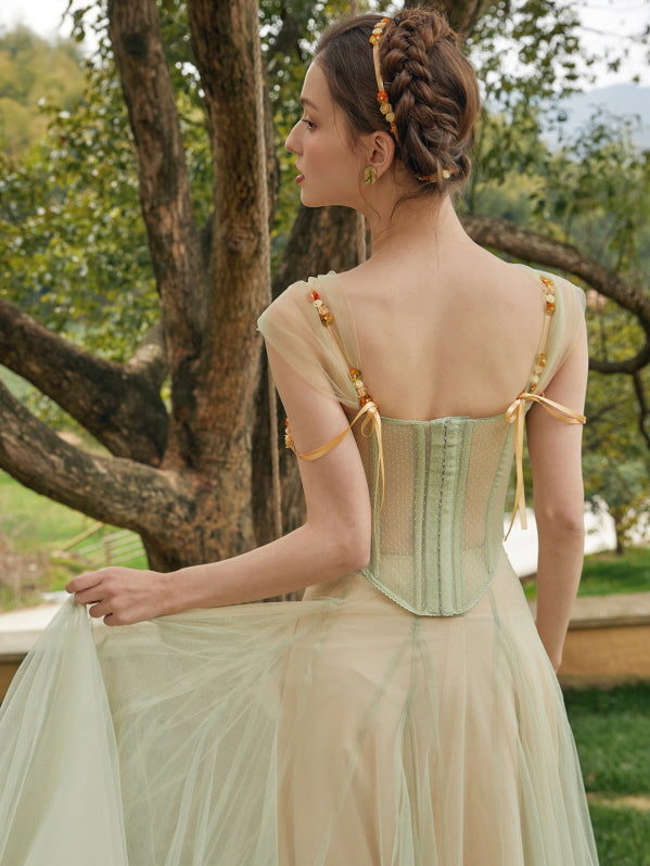 A woman shows the elegant back of a fairycore corset dress with ribbon shoulder ties and flowing tulle skirt in a soft, woodland setting.