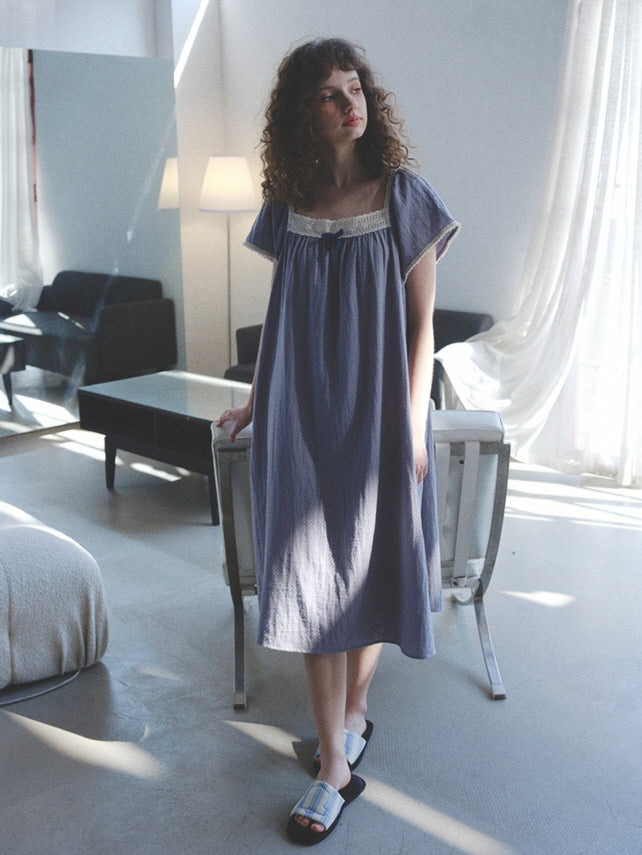 The model stands quietly in soft light wearing a lavender cotton nightgown with lace neckline, styled for a relaxed and romantic cottagecore morning.