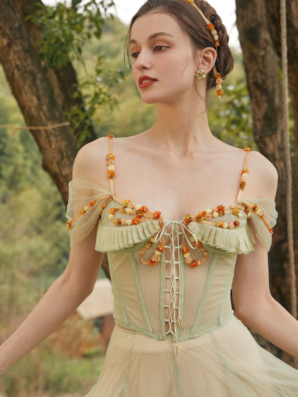 Close-up of a model smiling softly in a green vintage-inspired corset dress decorated with floral bead details and sheer off-shoulder straps.