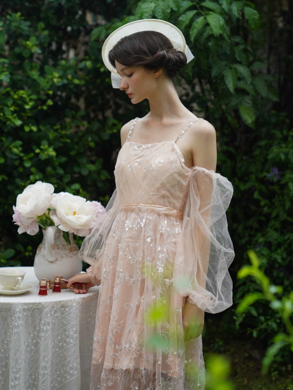 Back view of the model walking away from a tea table in a blush embroidered dress with ribbon waist detail and floral hat, evoking fairycore charm.