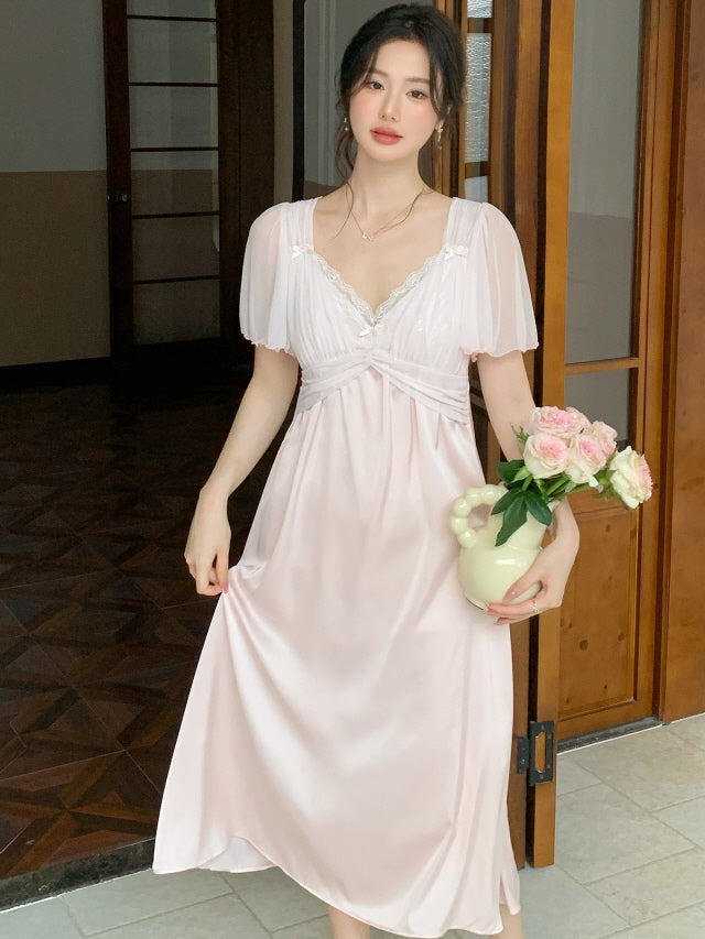 Wearing a pastel pink fairycore loungewear dress, the model holds a vase of roses in a softly lit hallway, capturing a delicate and romantic morning mood.