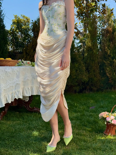 Cream ruched satin midi skirt with soft sheen, styled with a floral embroidered corset top in a romantic garden setting – fairytale-inspired elegant women’s outfit