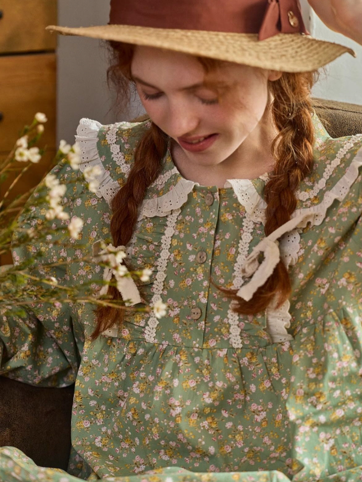 A playful moment in a green floral dress adorned with lace trim and bow accents, styled with a straw hat for a dreamy, nostalgic vibe.