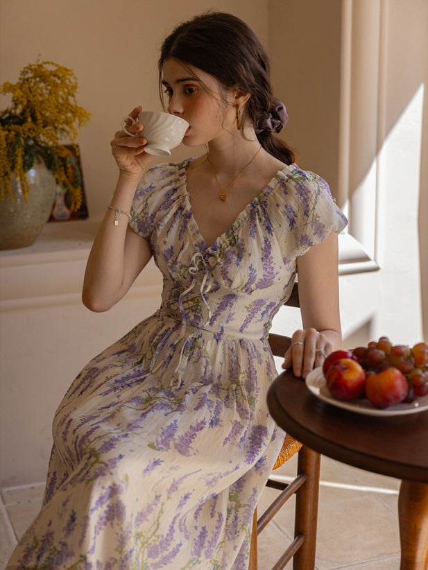 Woman in a lavender floral dress sipping tea by the window, capturing a serene cottagecore vibe with soft, natural lighting and vintage-inspired details.